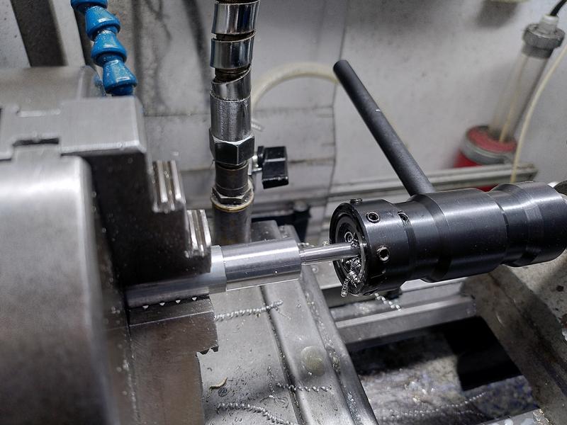 A piece of aluminium held in a 3 jar chuck on a metal lathe. I thas a
diameter turned, and then a much smaller section. This section is being
threaded with a blued steel tail stock die holder.