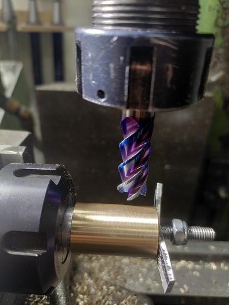 A close up of the end of an ER32 ollet block, an aluminium arbor holds a
bronze part. There is a bet aluminium bar held in place with a nyloc nut
on the end. A purply colourd end mill is in the spindle on the far side of
the part.