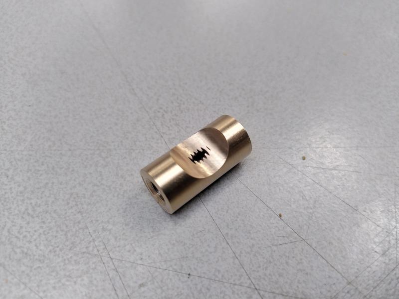A small brass cylinder laying on a grey table. A scallop has been cut
out the side, and the thread through the middle is visible in the middle
of the scallop.
