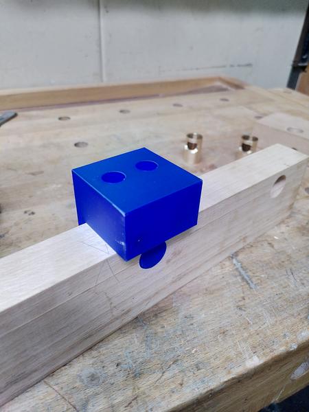 A piece of beech wood (fagus sylvatica) with a 3d printed blue PLA
drilling guide sitting on top. Part of the drill guide is inserted into
a hole in the beech. There's a second hole further along.