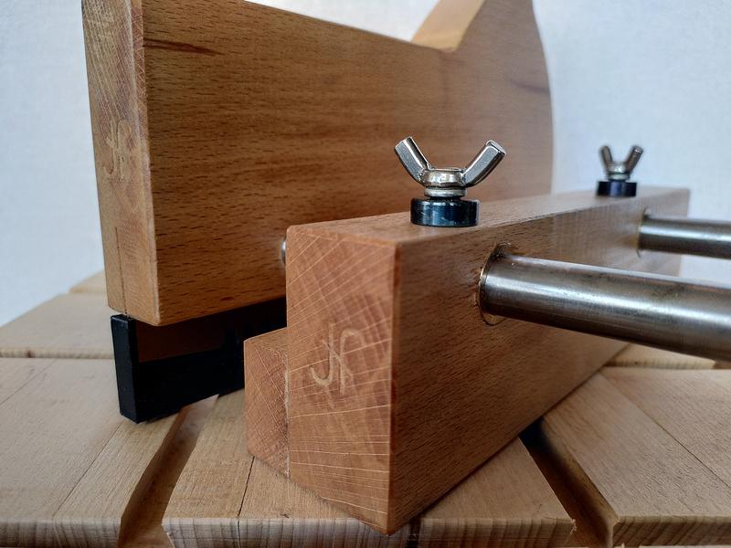 Close up of the front of the fence of a wooden kerfing plane. The wood
has a dark oiled finish. There's an ambigram JF makers mark stamped in the
end. The washer under the wingnut on top of the fence is a dark blue. The
arms are steel.